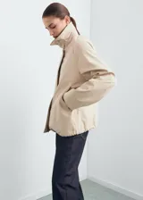 Chaqueta oversize color beige con cuello camisero de pana en contraste color negro. Presenta cierre frontal oculto con cremallera y botones, manga larga y bajo con cordón interior ajustable.