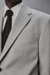 Blazer slim fit de color gris, con cuello de solapas de muesca, cierre frontal de dos botones, bolsillos laterales con solapa y bolsillo de vivo en el pecho. Presenta mangas largas con botones en los puños y aberturas en la espalda.