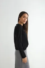 Sweater de punto negro con cuello redondo y detalle de borde ondulado, de manga larga y corte clásico.