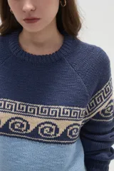 Sweater de tejido de punto con diseño jacquard, cuello redondo y mangas largas. Presenta una combinación de bloques de color azul marino y celeste con un patrón geométrico en la parte superior.