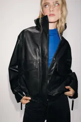 Cazadora de piel 100% color negro de Zara Woman Collection, con cuello subido, manga larga y bolsillos de plastrón con solapa en el delantero. Cuenta con bajo elástico y cierre frontal con cremallera y botones a presión ocultos.