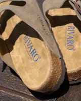Sandalias tipo zueco marca Rivaro, confeccionadas en cuero gamuzado color beige. Presentan dos tiras anchas con hebilla metálica, plantilla anatómica de corcho y látex, y suela de goma antideslizante.