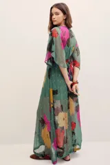Vestido largo verde con estampado floral multicolor, escote en V cruzado, mangas amplias tipo capa y detalles metalizados.