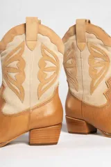 Bota texana de cuero color marrón claro con detalles en beige. Diseño con puntera en punta y caña media con bordados decorativos. Taco bajo de madera.