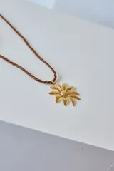Collar con tiento trenzado blanco y dije metálico dorado con forma de sol estilizado.