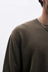 Buzo de tejido de punto color marrón oscuro, con cuello redondo y manga larga. Presenta una textura acanalada vertical.