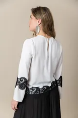 Blusa color marfil de seda con incrustaciones de cruni negro, mangas amplias y cuello cerrado con abertura.