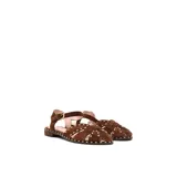 Sandalias chatitas de cuero en color marrón tostado, con diseño de tiras cruzadas en el empeine decoradas con tachas metálicas pequeñas. Cuenta con tira ajustable al tobillo mediante hebilla metálica y taco bajo.