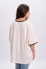 Remera oversize de manga corta en color crudo, con cuello redondo y puños en tono marrón oscuro. Cuenta con el texto "Los Angeles" estampado en el frente.