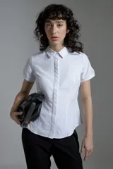 Camisa blanca de corte clásico, con cuello camisero, mangas cortas y cierre frontal con botones.