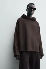 Sudadera de corte boxy fit en color marrón oscuro, con capucha, mangas largas y bandas laterales a contraste. Presenta un diseño de bajo con acabado irregular deshilachado.