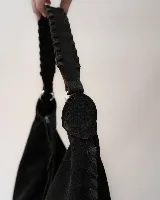 Bolso tipo hobo de gran tamaño, confeccionado en gamuza color marrón oscuro. Presenta un diseño artesanal con costuras visibles y detalles de tientos en el cuerpo, asa integrada con pespuntes a mano y cierre superior.