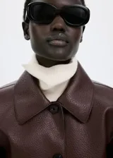 Chaqueta de cuero sintético marrón con cuello camisero, cierre frontal de botones oscuros y bolsillos frontales de parche con solapa.