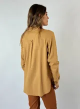 Camisa color mostaza con volados desflecados a lo largo de la botonadura frontal, cuello mao y mangas largas con puños abotonados.