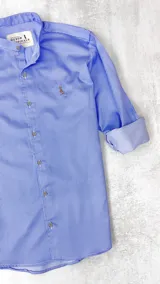 Camisa celeste con rayas verticales blancas, cuello mao y mangas largas con puños abotonados.
