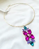 Gargantilla rígida dorada con dije colgante de piedras facetadas en forma de lágrima color fucsia, lila y turquesa.