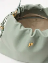 Cartera marrón de cuero vacuno liso con correa regulable y aplique JCH en el frente. Sistema de ajuste mediante tiras.