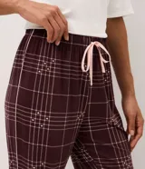 Pantalón de pijama tipo jogger confeccionado en tejido peach touch de color bordó, con estampado de cuadros y pequeños detalles de corazones. Posee cintura elástica con cordón de ajuste en color rosado y puños elastizados en los tobillos.