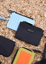 Billetera y tarjetero celeste con cierre superior, correa de muñeca incorporada y aplique metálico con logo frontal.