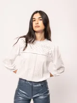 Blusa blanca de algodón con escote redondo, manga tres cuartos y silueta oversized. Presenta bordados y texturas combinadas.