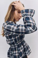 Blusa de manga larga con diseño a cuadros escoceses en tonos azul marino, blanco y naranja. Presenta cuello redondo, hombros ligeramente abullonados y detalle de fruncido elástico en la cintura que crea un efecto peplum.
