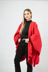 Capa de paño color rojo con corte amplio y caída natural. Presenta detalles de dijes metálicos en baño de oro distribuidos en la espalda y una etiqueta de cuero con el logo de la marca en la parte superior.