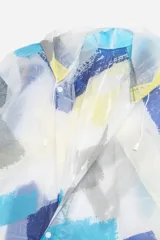 Piloto impermeable de corte recto y largo midi, con capucha ajustable mediante cordones. Presenta un diseño estampado con motivos botánicos en tonos verdes y amarillos sobre una base translúcida. Cuenta con cierre frontal mediante botones a presión y mangas largas.