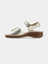 Sandalia de cuero con tiras ajustables de velcro en el empeine y el talón. Presenta un diseño bicolor en tonos dorado y beige, con una suela de goma texturizada de aspecto natural.