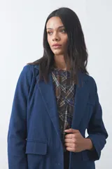 Blazer de jean azul con silueta recta y corte sastrero. Presenta solapas clásicas, bolsillos frontales con tapa, cierre con botones forrados y detalles de botones en los puños.