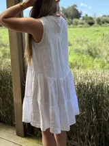 Vestido celeste de lino, sin mangas, con cuello mao y botones de nácar. Presenta varios cortes en su largo, aportando movimiento y un toque moderno a este diseño fresco y elegante.