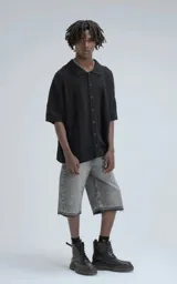 Camisa de manga corta tejida en punto abierto negro, con cuello polo y cierre frontal de botones. Presenta un calce oversize.