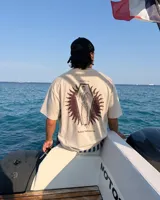Remera oversize color beige de corte holgado, con estampa en la espalda que representa un esqueleto dentro de un ataúd con rayos oscuros y texto descriptivo.