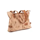 Cartera tipo shopper de cuero color marrón tostado, con doble asa de hombro, costuras decorativas centrales, detalles de tiras laterales con hebilla y un parche de cuero con logo grabado en la parte frontal.