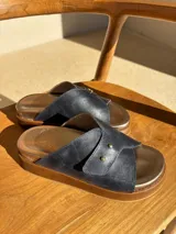 Sandalia de cuero con diseño de tiras cruzadas en color azul oscuro, detalle de doble remache dorado y plataforma de madera con plantilla metalizada.