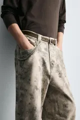 Pantalón de corte relajado confeccionado en algodón, con diseño de efecto lavado y estampado abstracto en tonos grises y beige. Presenta cinco bolsillos y cierre frontal con cremallera y botón.