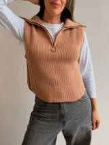 Chaleco de tejido de punto acanalado en color camel, con cuello polo, medio cierre frontal y aberturas laterales con detalle de botones.