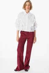 Camisa de corte cropped en color azul, con cuello clásico y cierre frontal de botones. Presenta volados decorativos que recorren la parte frontal y las mangas largas, terminando en puños abotonados.