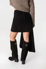 Falda de cuero marrón con diseño asimétrico, presenta un detalle de lazo frontal drapeado que crea una caída lateral más larga.