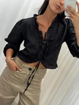 Blusa negra de lino con acabado brillante, de manga larga abullonada, escote con volados y cierre frontal con tiras para anudar.