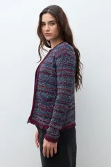 Chaqueta de tejido de punto con textura, diseño multicolor en tonos azul, rojo y blanco. Presenta cuello redondo, cierre frontal y detalles de flecos en los bordes y puños.
