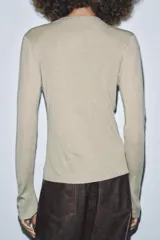 Chaqueta de punto color beige claro, manga larga y cuello redondo. Presenta un detalle de frunces verticales ajustados por botones a tono en el centro frontal.