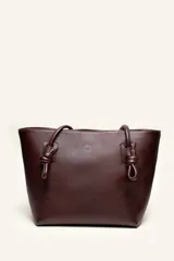 Cartera tote de cuero suave color marrón, con diseño amplio y líneas simples, con tiras de hombro decoradas con nudos artesanales y pequeño logo grabado en el centro.