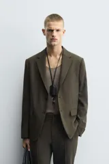 Blazer de corte slim fit en color verde oscuro, con cuello de solapas de muesca, cierre frontal de un botón, bolsillos laterales con solapa y bolsillo de vivo en el pecho.