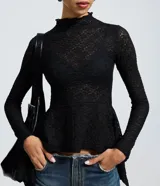 Blusa de encaje floral negro con cuello alto y mangas largas. Presenta un diseño ajustado en el torso con un detalle peplum en el ruedo que aporta volumen y movimiento.