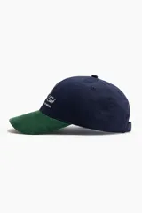 Gorra confeccionada en sarga de algodón azul marino con visera de pana verde oscuro. Presenta bordado frontal con texto y monograma en hilo blanco.