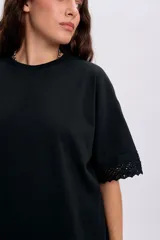 Remera negra de manga corta con detalles de encaje en el ruedo y las terminaciones de las mangas, de corte holgado y cuello redondo.