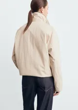 Chaqueta oversize color beige con cuello camisero de pana en contraste color negro. Presenta cierre frontal oculto con cremallera y botones, manga larga y bajo con cordón interior ajustable.