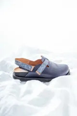 Zuecos de cuero azul con suela negra y tira trasera ajustable con hebilla.