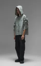 Campera rompevientos de diseño oversize, color verde, confeccionada en microfibra técnica ligera. Presenta capucha integrada, cierre frontal técnico y un sistema de frunces elásticos regulables a lo largo de las mangas que permiten ajustar el volumen de la prenda.
