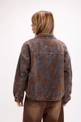 Campera de jean con diseño de estampado paisley en tonos marrones y grises. Presenta un corte relajado, cuello camisero, cierre frontal con botones metálicos y bolsillos frontales con solapa.